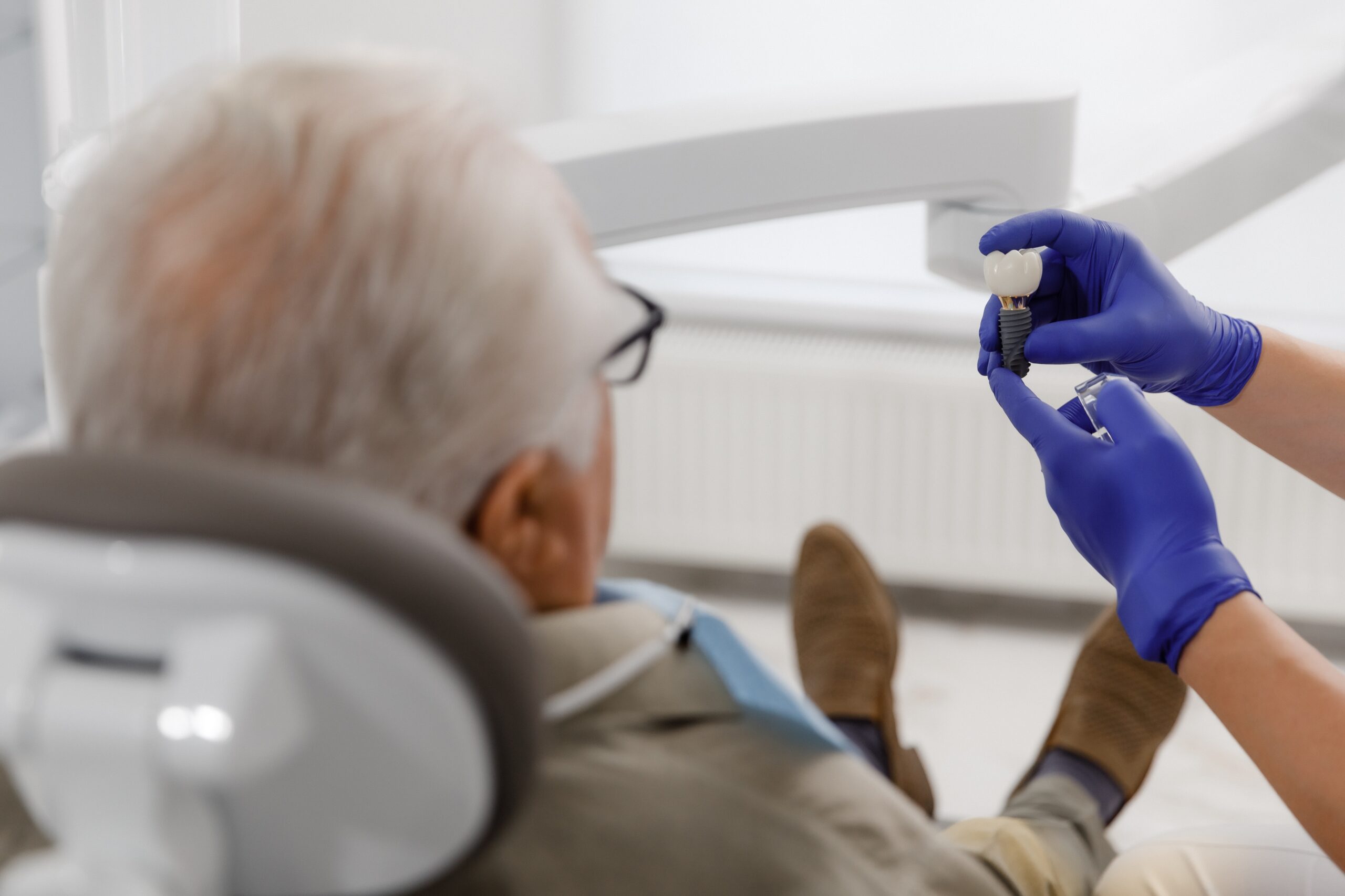 Dentist showing a dental implant and crown to a patient during a consultation
